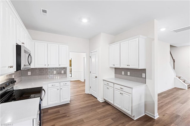 kitchen featuring visible vents, wood finished floors, stainless steel appliances, white cabinets, and light countertops