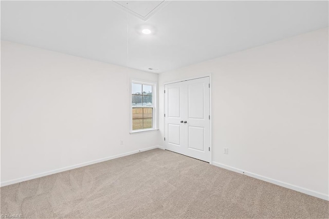 empty room featuring attic access, carpet flooring, and baseboards