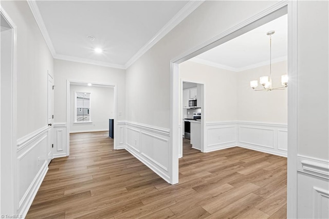 corridor with crown molding, a decorative wall, light wood-style floors, and a chandelier