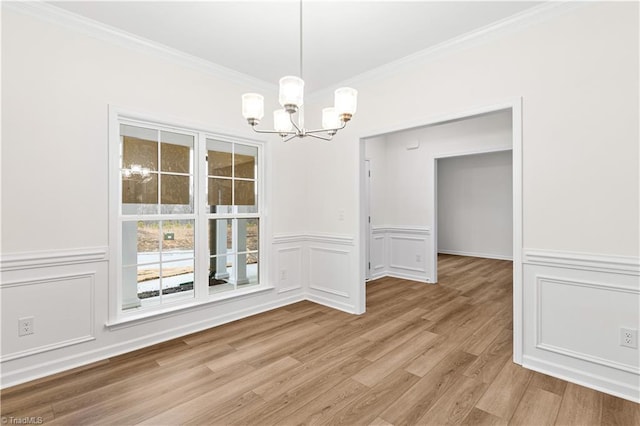 unfurnished dining area featuring a wainscoted wall, an inviting chandelier, ornamental molding, light wood-style floors, and a decorative wall