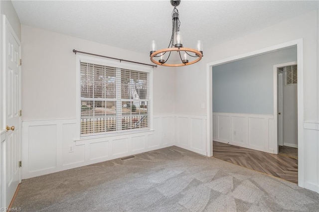 carpeted spare room featuring a textured ceiling and an inviting chandelier