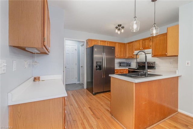 kitchen with appliances with stainless steel finishes, decorative light fixtures, kitchen peninsula, and light wood-type flooring