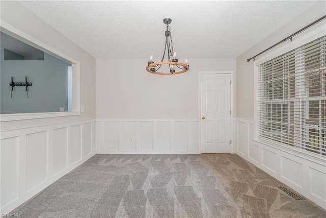 spare room with light carpet, a textured ceiling, and a chandelier