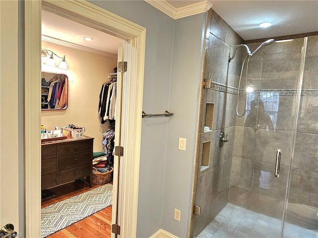 full bathroom with a spacious closet, wood finished floors, a shower stall, and crown molding