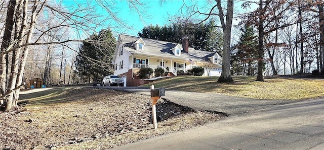 cape cod home featuring driveway and covered porch