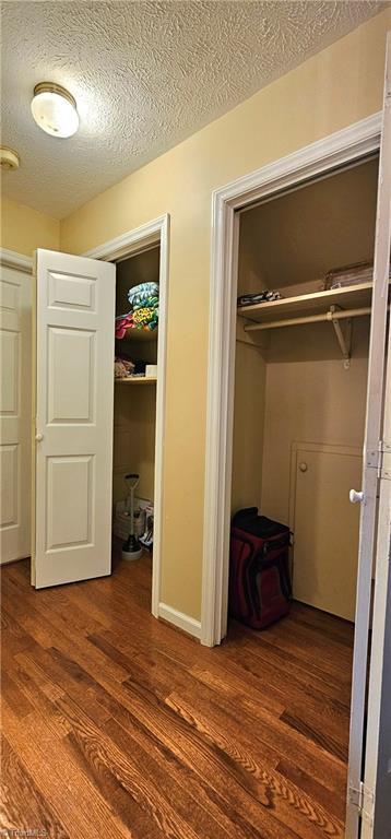 unfurnished bedroom with a textured ceiling, wood finished floors, and two closets