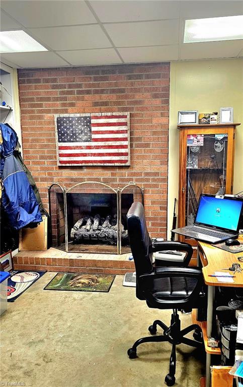 office space with concrete flooring, a drop ceiling, and a brick fireplace