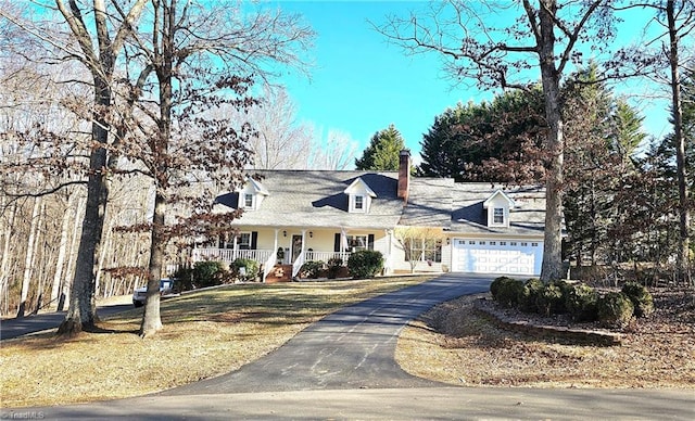 new england style home with covered porch, driveway, an attached garage, and a front yard