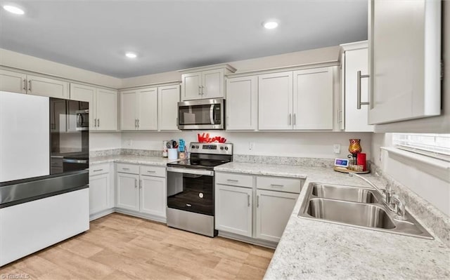 kitchen with appliances with stainless steel finishes, a sink, light countertops, recessed lighting, and light wood-style flooring