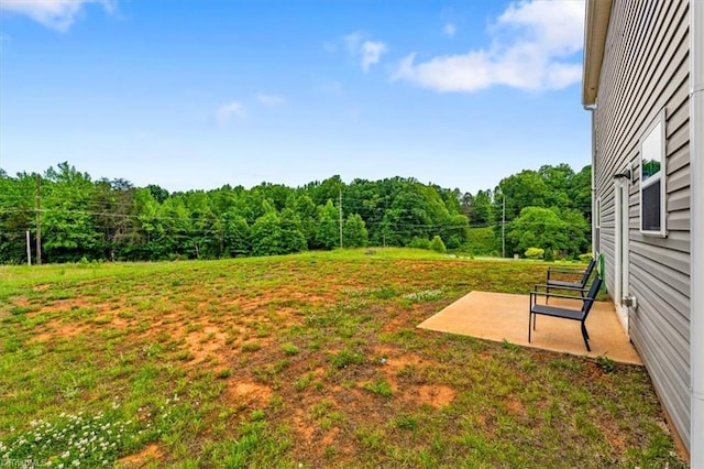 view of grassy yard featuring a wooded view and a patio area