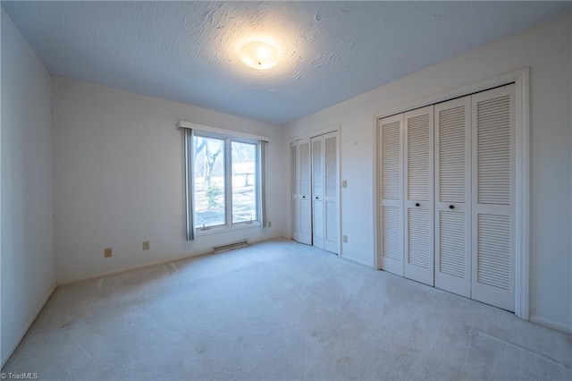 unfurnished bedroom with two closets, light carpet, and a textured ceiling