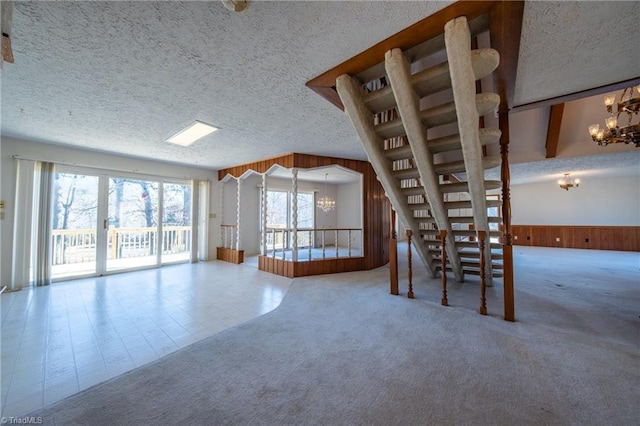 unfurnished dining area with wooden walls, a textured ceiling, a chandelier, and carpet