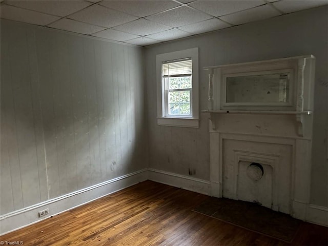 unfurnished room with a drop ceiling, wood walls, and wood-type flooring