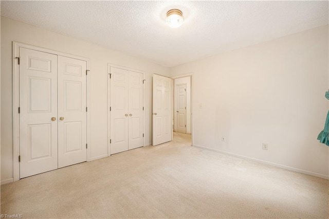 unfurnished bedroom with a textured ceiling, two closets, and light colored carpet