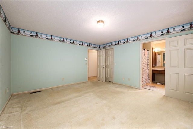 unfurnished bedroom with ensuite bath, carpet flooring, and a textured ceiling