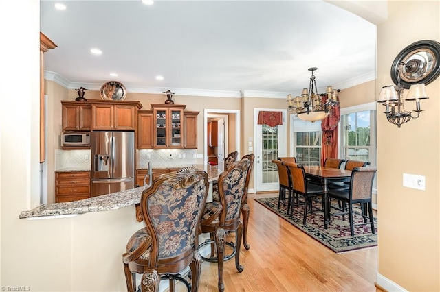 kitchen with stainless steel refrigerator with ice dispenser, brown cabinetry, a chandelier, a breakfast bar area, and glass insert cabinets