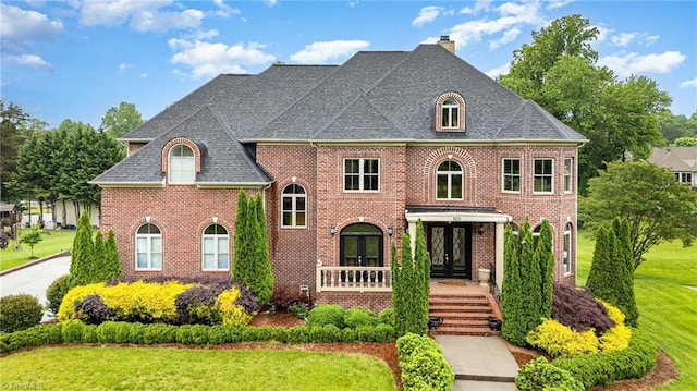view of front of house featuring french doors, brick siding, a front yard, a chimney, and covered porch