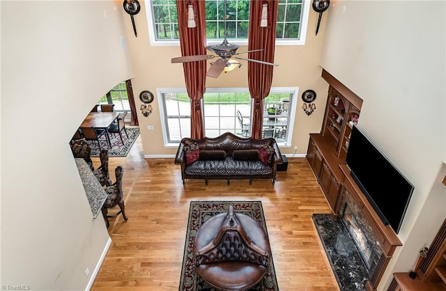living area featuring a towering ceiling, wood finished floors, ceiling fan, and baseboards