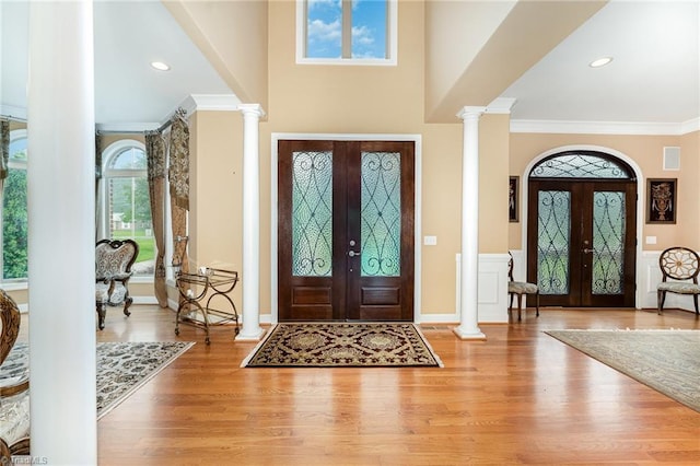 foyer entrance with french doors, ornate columns, ornamental molding, and wood finished floors