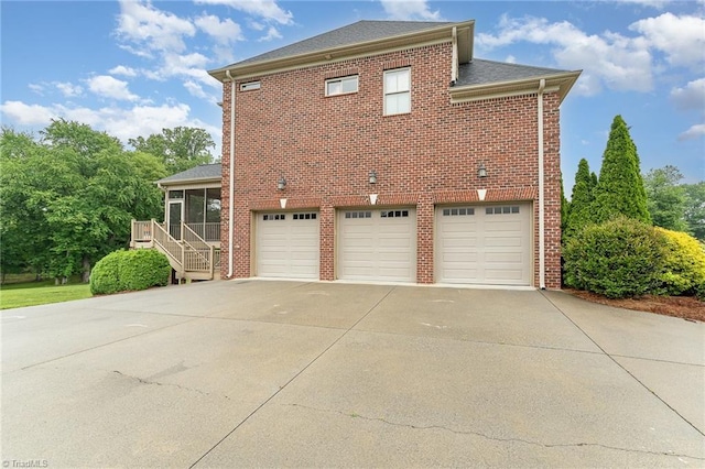 view of side of property with a sunroom, driveway, a garage, brick siding, and stairs