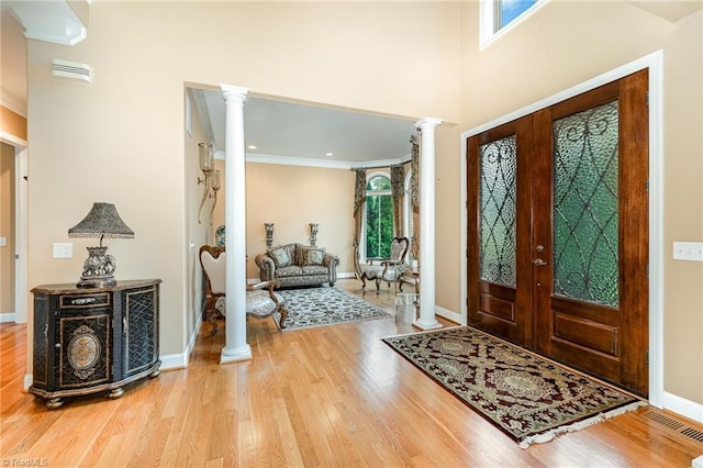 foyer with ornate columns, wood finished floors, french doors, and ornamental molding