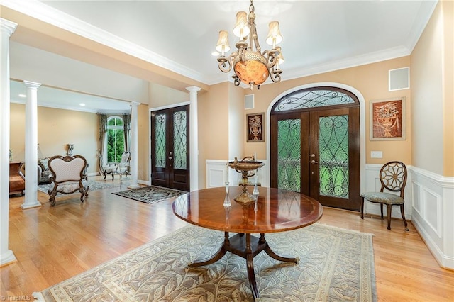 entrance foyer with decorative columns, french doors, light wood finished floors, a chandelier, and ornamental molding