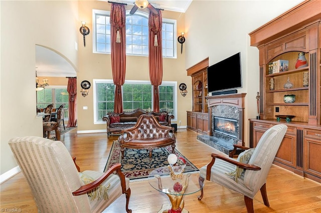living area featuring a premium fireplace, a towering ceiling, baseboards, light wood-type flooring, and arched walkways