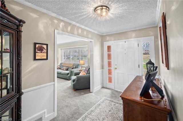 carpeted entrance foyer with ornamental molding, a wainscoted wall, and a textured ceiling