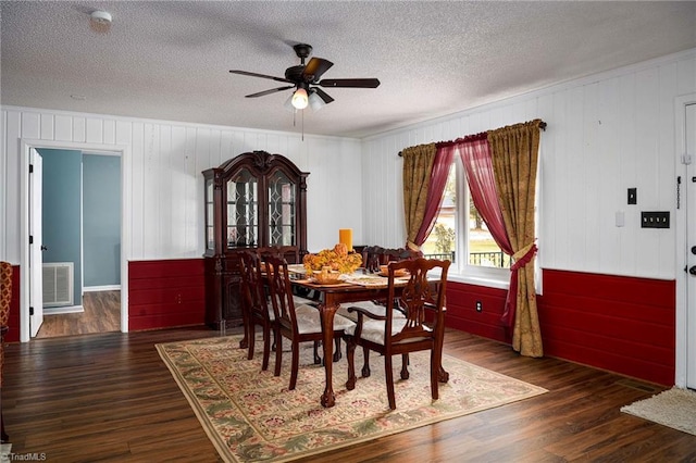 dining area with dark wood-type flooring, ceiling fan, a textured ceiling, and wooden walls