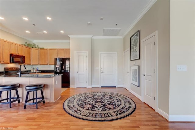 kitchen with a breakfast bar area, light brown cabinets, light wood finished floors, black appliances, and dark countertops