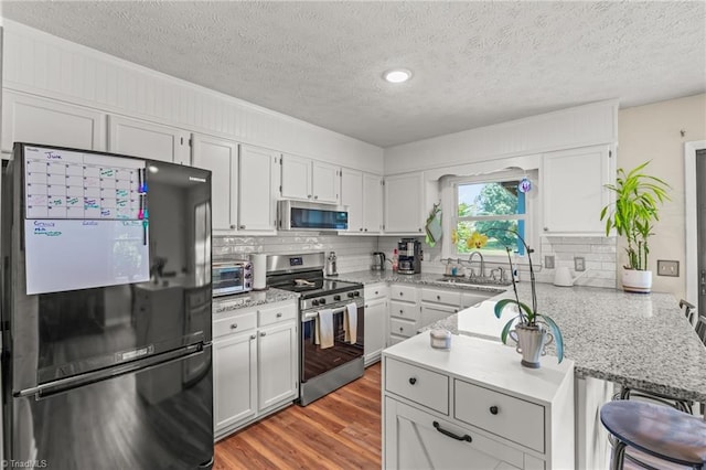 2664 Old Thomasville Rd, Winston-Salem, NC 27107 - kitchen featuring stainless steel appliances, a peninsula, decorative backsplash, light wood-style flooring, and a textured ceiling