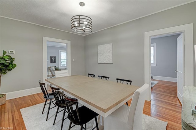 dining space featuring a chandelier, baseboards, light wood-style flooring, and ornamental molding
