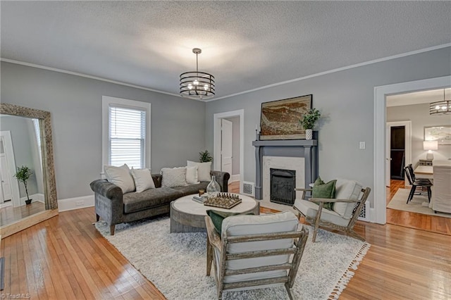 living room with a chandelier, light wood-style flooring, a fireplace with flush hearth, ornamental molding, and a textured ceiling