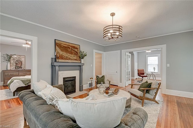 living room with a high end fireplace, light wood finished floors, a textured ceiling, ornamental molding, and baseboards