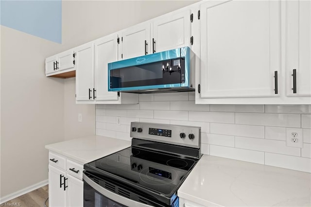 kitchen with white cabinets, appliances with stainless steel finishes, baseboards, wood finished floors, and backsplash