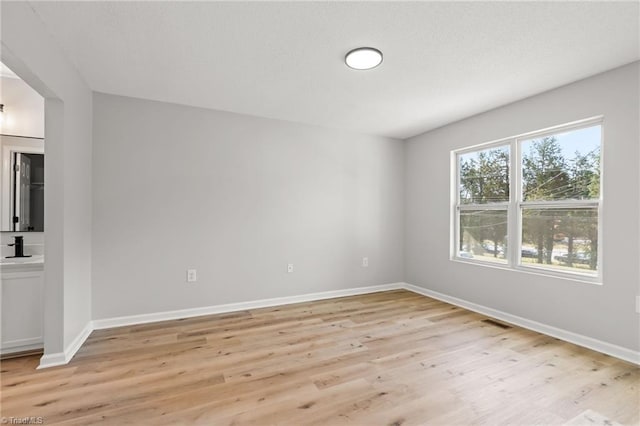 unfurnished room featuring a sink, baseboards, light wood-type flooring, and visible vents