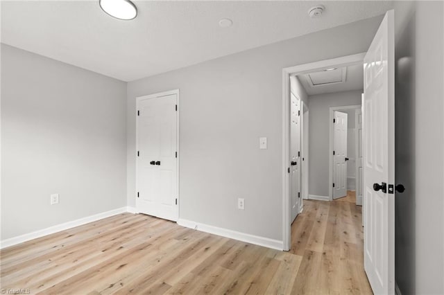 unfurnished bedroom with baseboards, attic access, and light wood-type flooring
