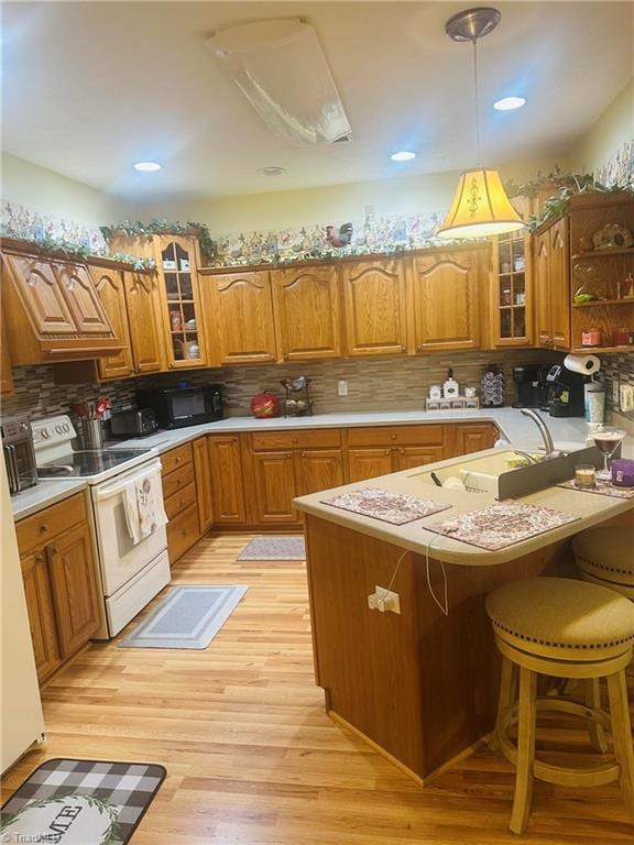 kitchen with white range with electric cooktop, black microwave, a peninsula, brown cabinets, and light wood finished floors