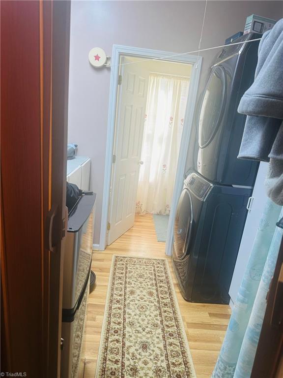 laundry room with light wood-type flooring and stacked washer and clothes dryer