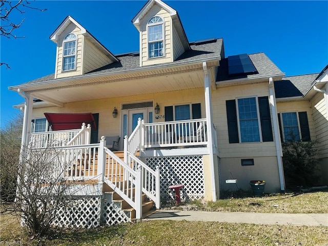view of front of house with a porch, a shingled roof, and solar panels