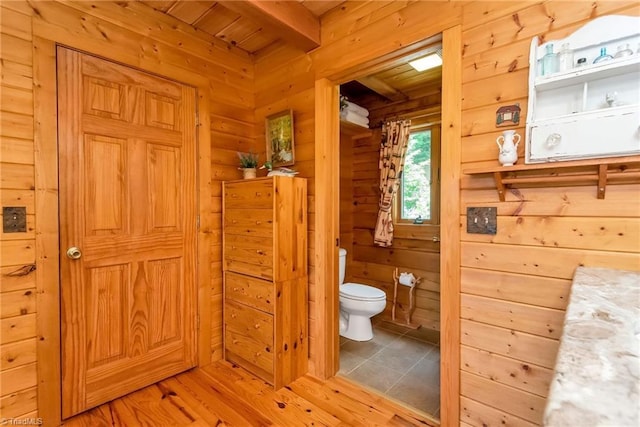 bathroom featuring beam ceiling, wood walls, toilet, and wood finished floors