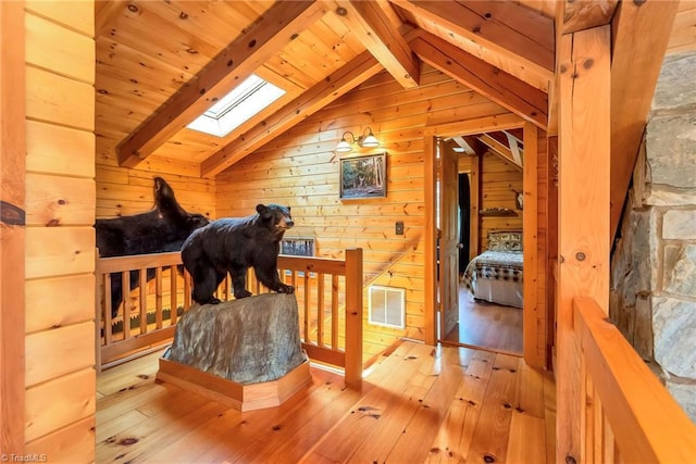 interior space featuring vaulted ceiling with skylight, wood walls, visible vents, and hardwood / wood-style flooring