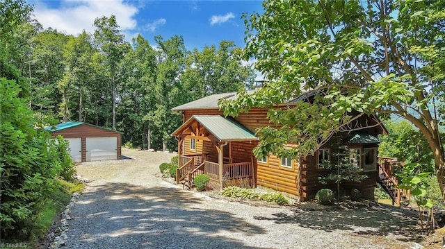 view of property exterior featuring a porch, metal roof, a detached garage, and an outdoor structure