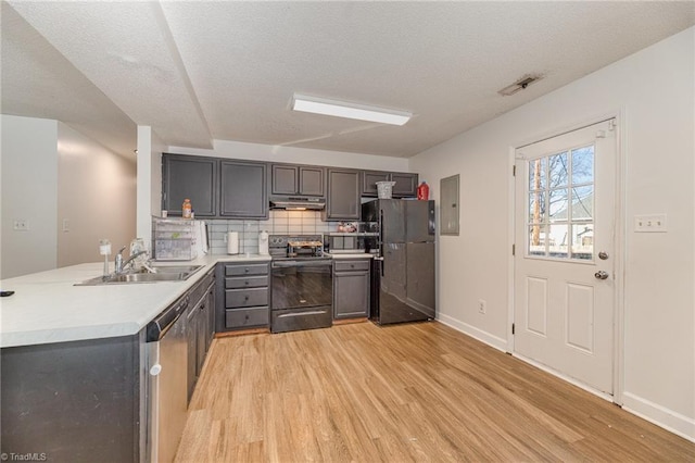 kitchen featuring a sink, black appliances, light countertops, under cabinet range hood, and light wood-type flooring