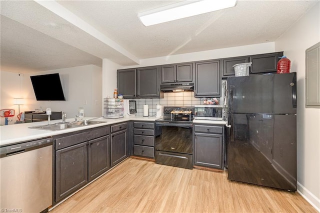 kitchen featuring light wood-type flooring, a sink, black appliances, under cabinet range hood, and tasteful backsplash