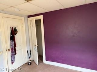 unfurnished bedroom with a closet, a drop ceiling, carpet flooring, and baseboards