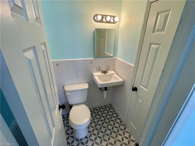 bathroom featuring tile patterned floors, toilet, sink, and tile walls