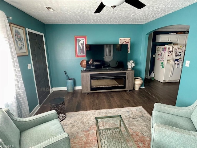 living room with dark hardwood / wood-style flooring, ceiling fan, and a textured ceiling