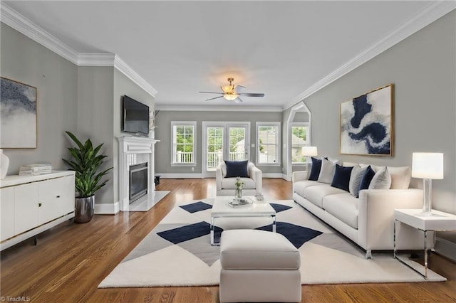 living area with baseboards, a fireplace with flush hearth, ceiling fan, ornamental molding, and wood finished floors