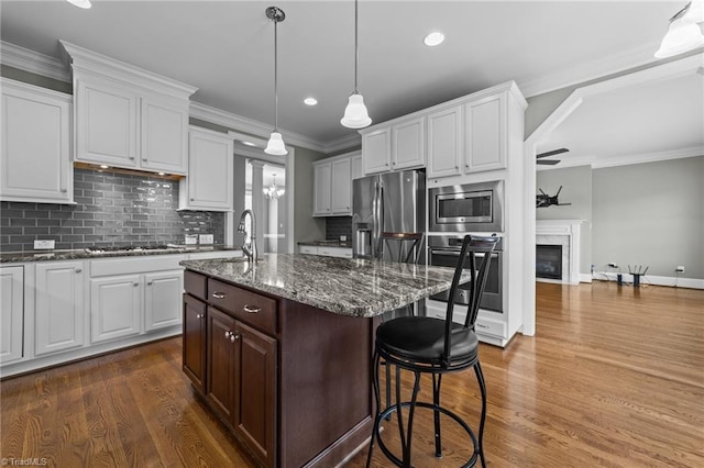 kitchen with a glass covered fireplace, appliances with stainless steel finishes, dark wood-style floors, a kitchen bar, and crown molding